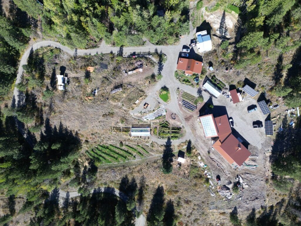 Top-down view of a homestead with solar panels, a greenhouse, garden beds and a gravel access road